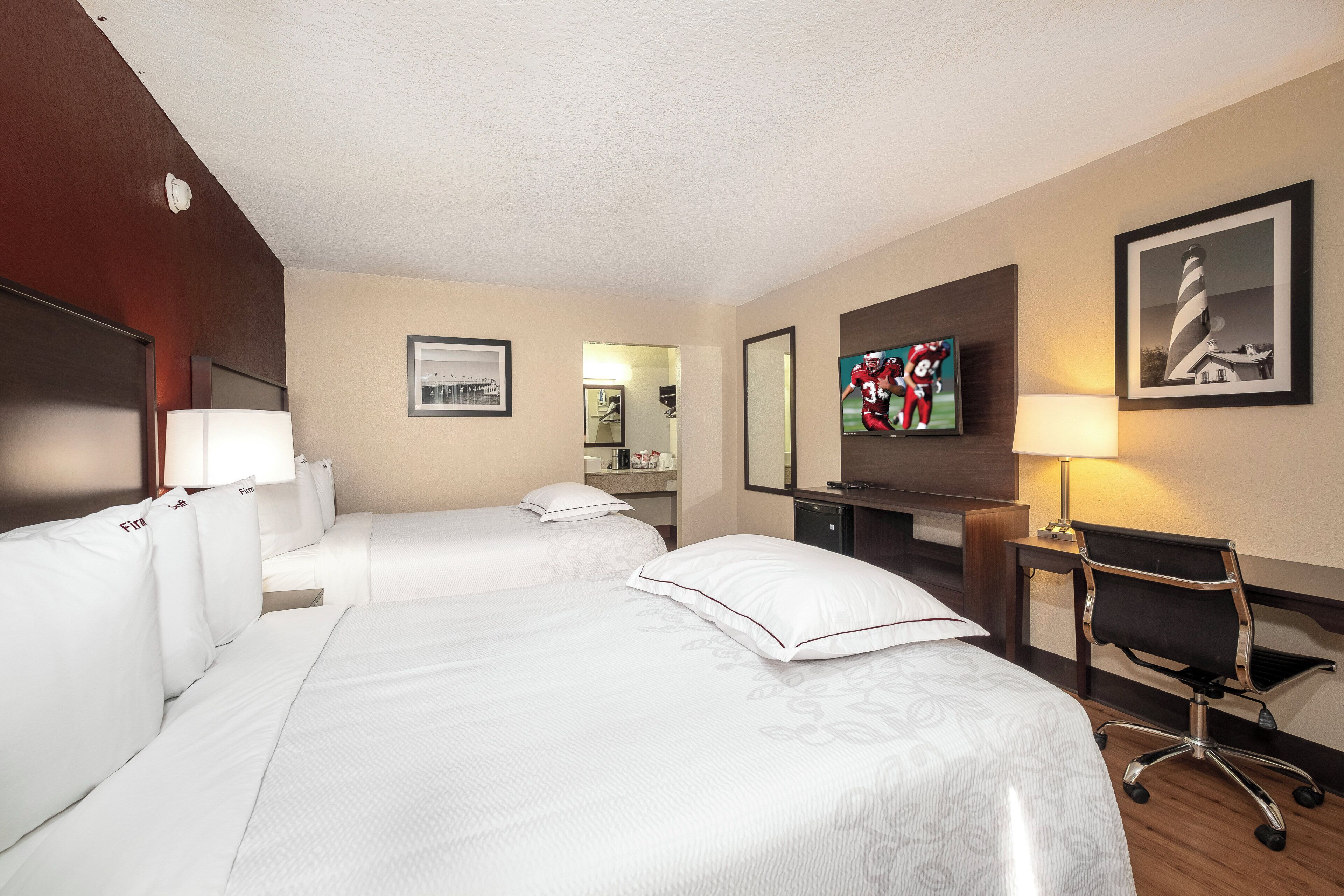 A hotel room with two beds, a desk, a chair, a television, and a framed picture on the wall.