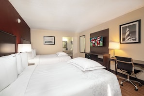 Une chambre d’hôtel avec deux lits, un bureau, une chaise, une télévision et un tableau encadré au mur.
