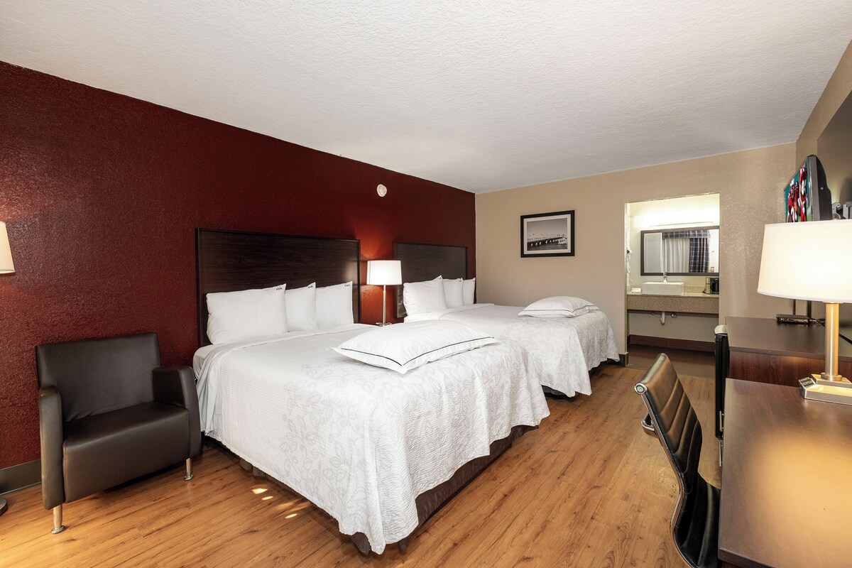 A hotel room with two beds, a desk, a chair, and a mirror.