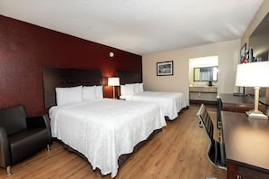 A hotel room with two beds, a desk, a chair, a lamp, and a mirror.