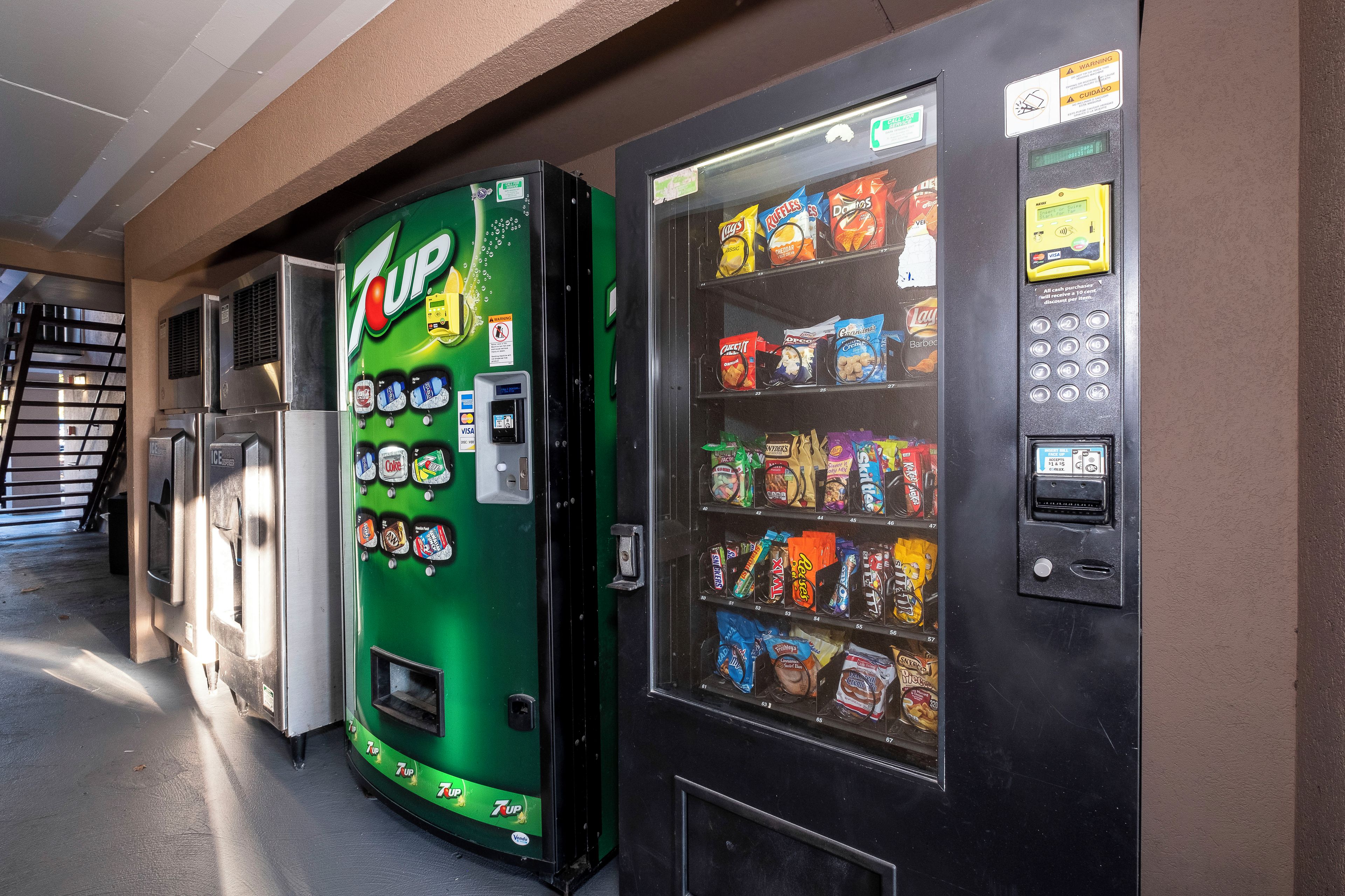 A 7UP vending machine and a snack vending machine with various snacks and drinks.