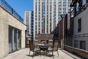 Un patio con una mesa redonda y sillas, un edificio de ladrillo y un edificio residencial alto al fondo.