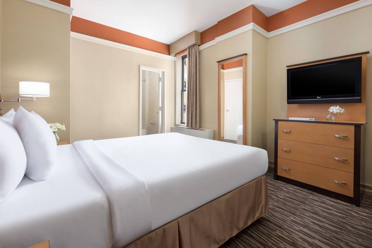 A hotel room with a large bed, a dresser, a flat-screen TV, and a window with curtains.