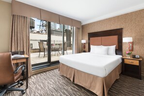 Habitación de hotel con una cama grande, un escritorio con silla, una pequeña mesa con sillas y vistas al balcón exterior.