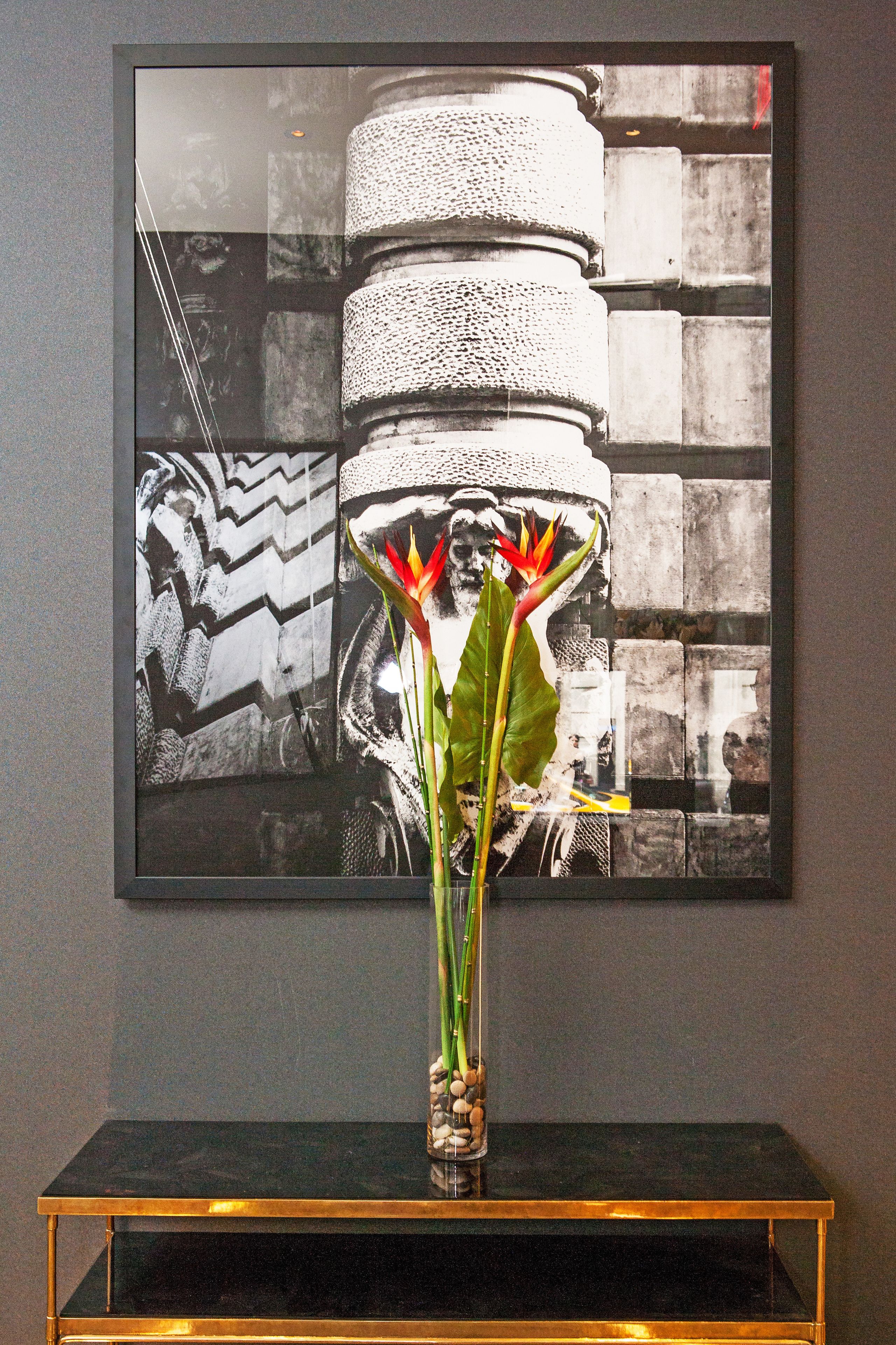 Une œuvre d’art encadrée représentant un vase de fleurs posé sur une console noire.