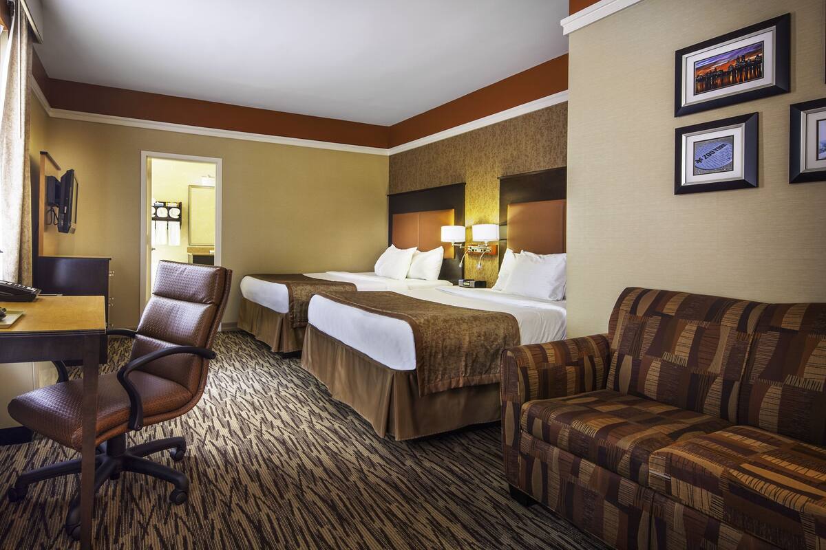 A hotel room with a bed, two bedside tables, a desk with a coffee maker, a chair, a sofa, and framed pictures on the wall.