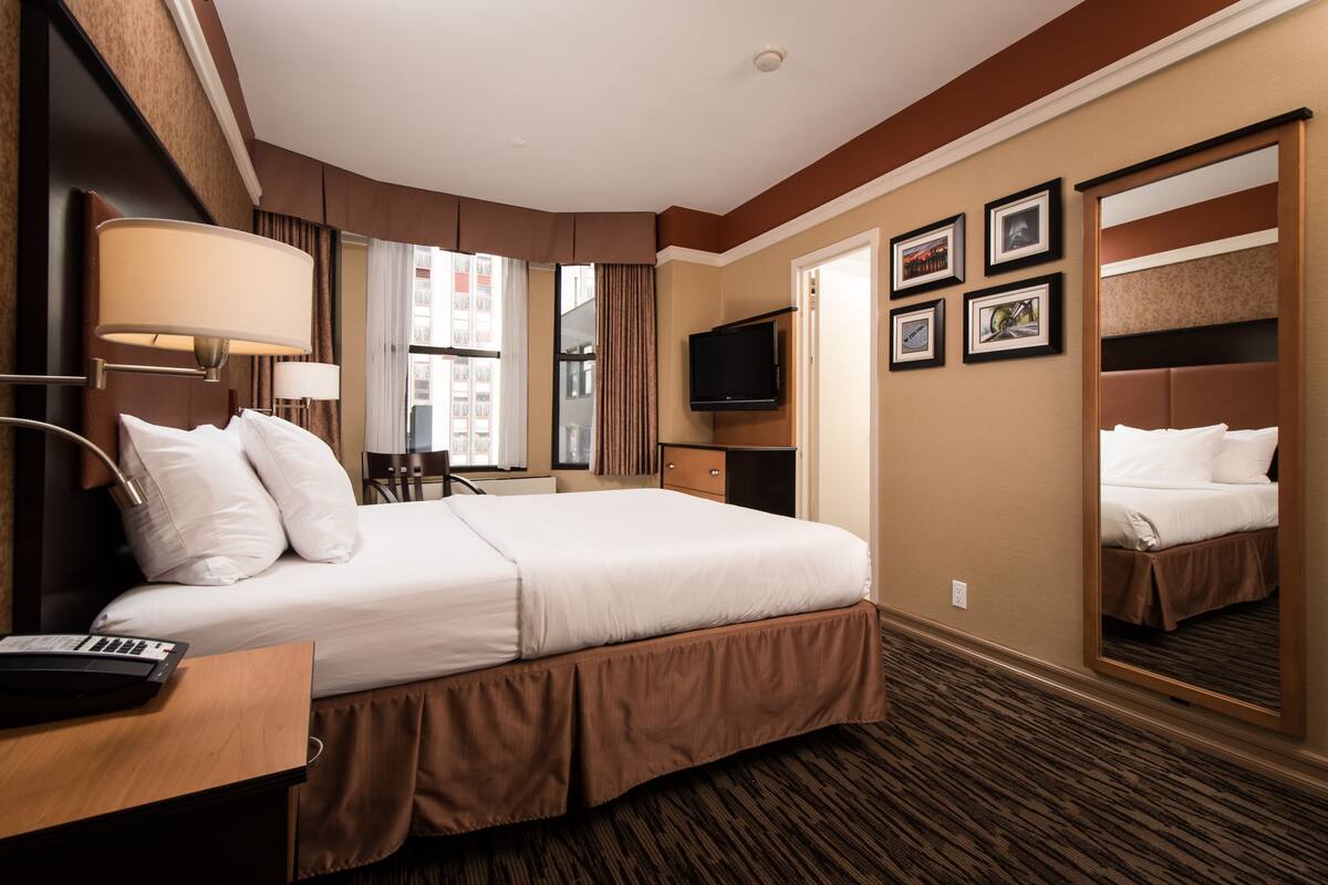 A hotel room with a large bed, a desk with a keyboard, a television, and a mirror.