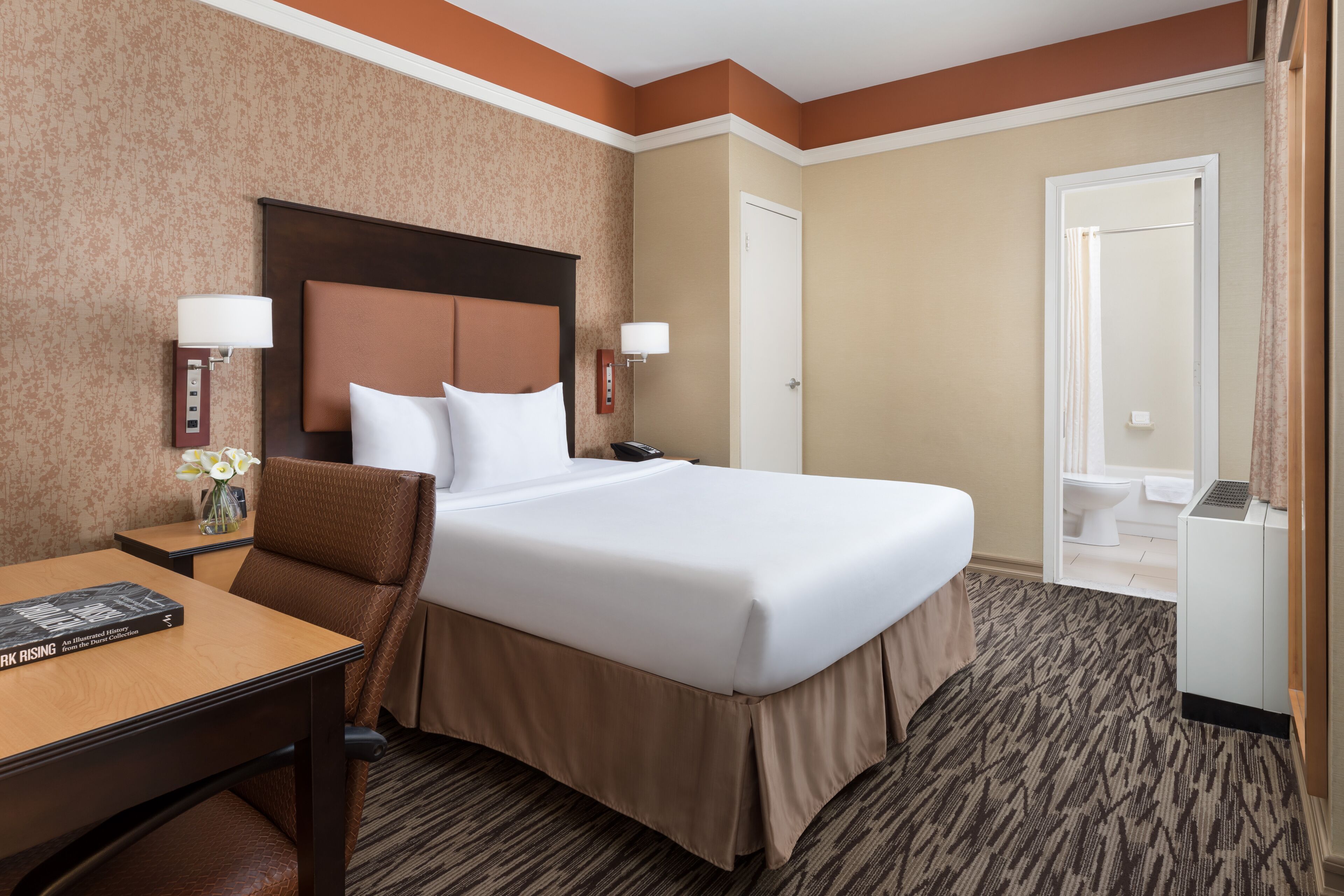 A hotel room with a large bed, a desk, a chair, and a bathroom visible through an open door.