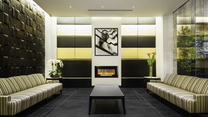 A modern living room with a fireplace, striped sofas, and a large wall with a geometric pattern. - The Hotel @ Fifth Avenue (New York)