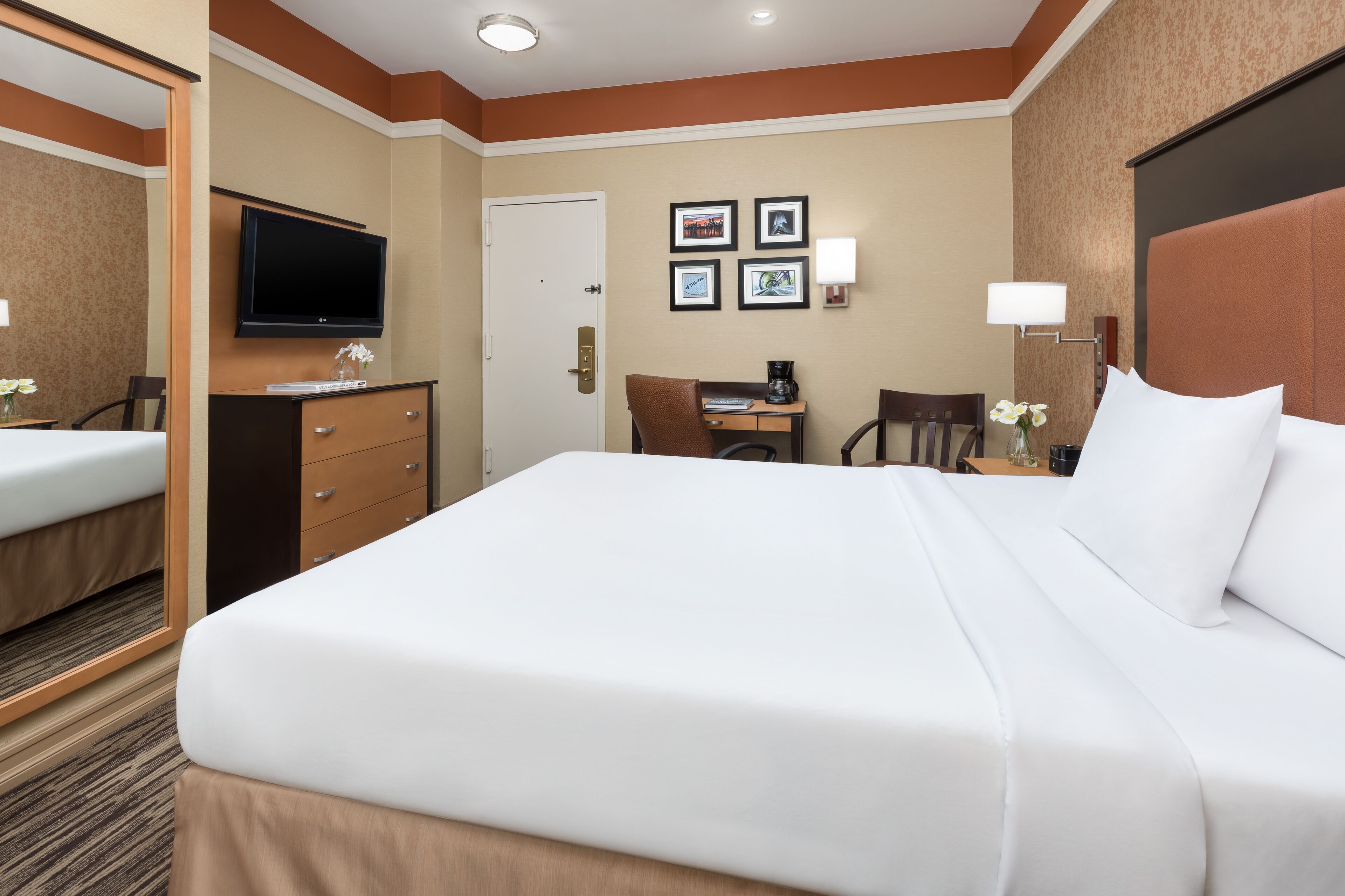 Habitación de hotel con una cama grande, un escritorio con silla, televisión y cuadros en la pared.