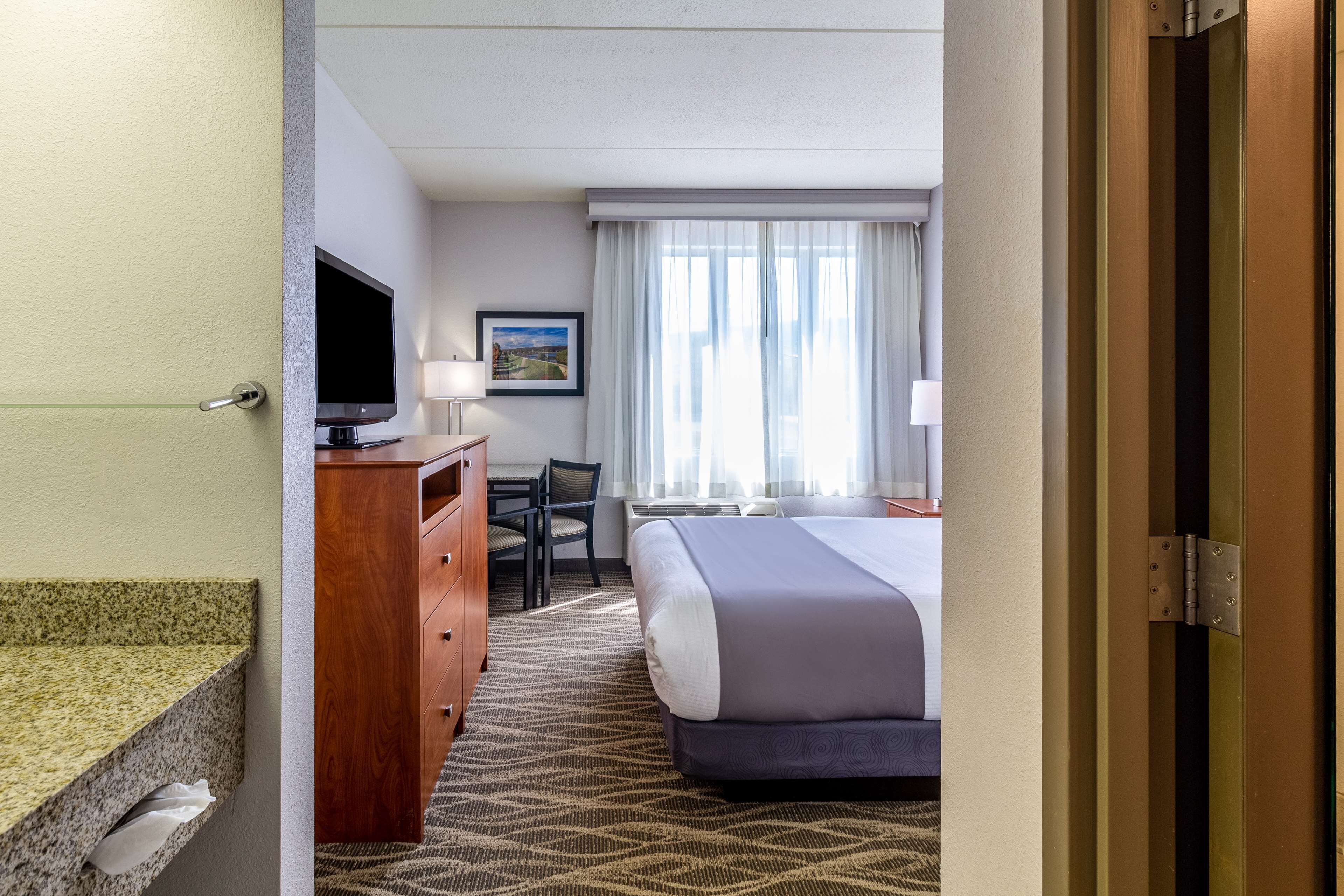 A hotel room with a bed, a desk, a chair, a television, and a window with curtains.