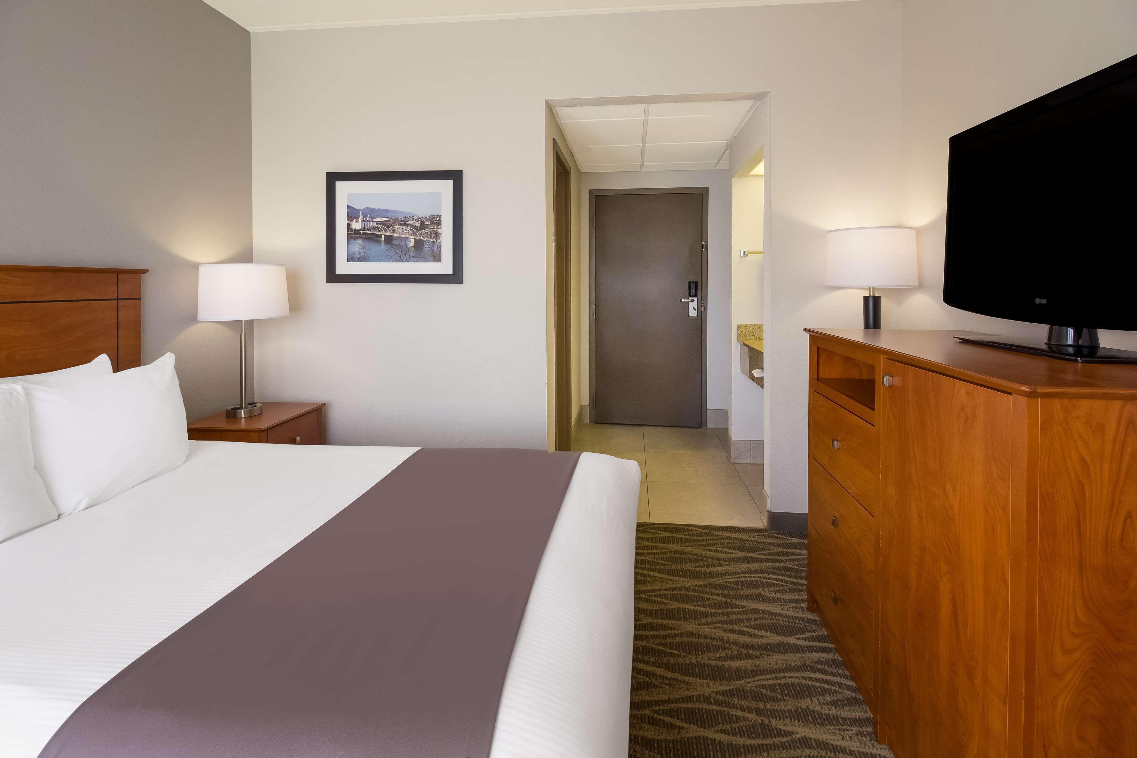 Habitación de hotel con una cama grande, un aparador de madera, un televisor y un cuadro en la pared.