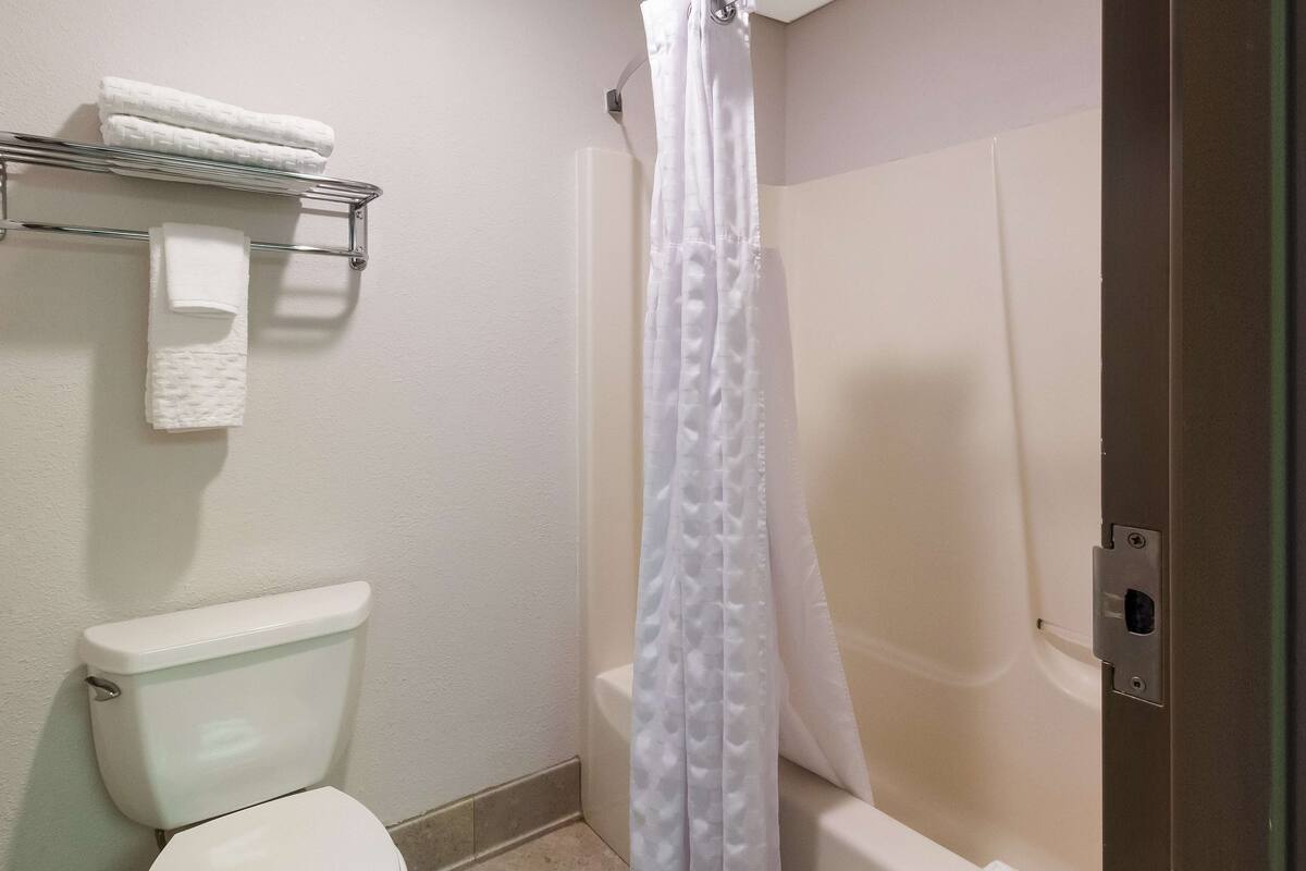 Un baño con inodoro, cortina de ducha y toallero con toallas dobladas.