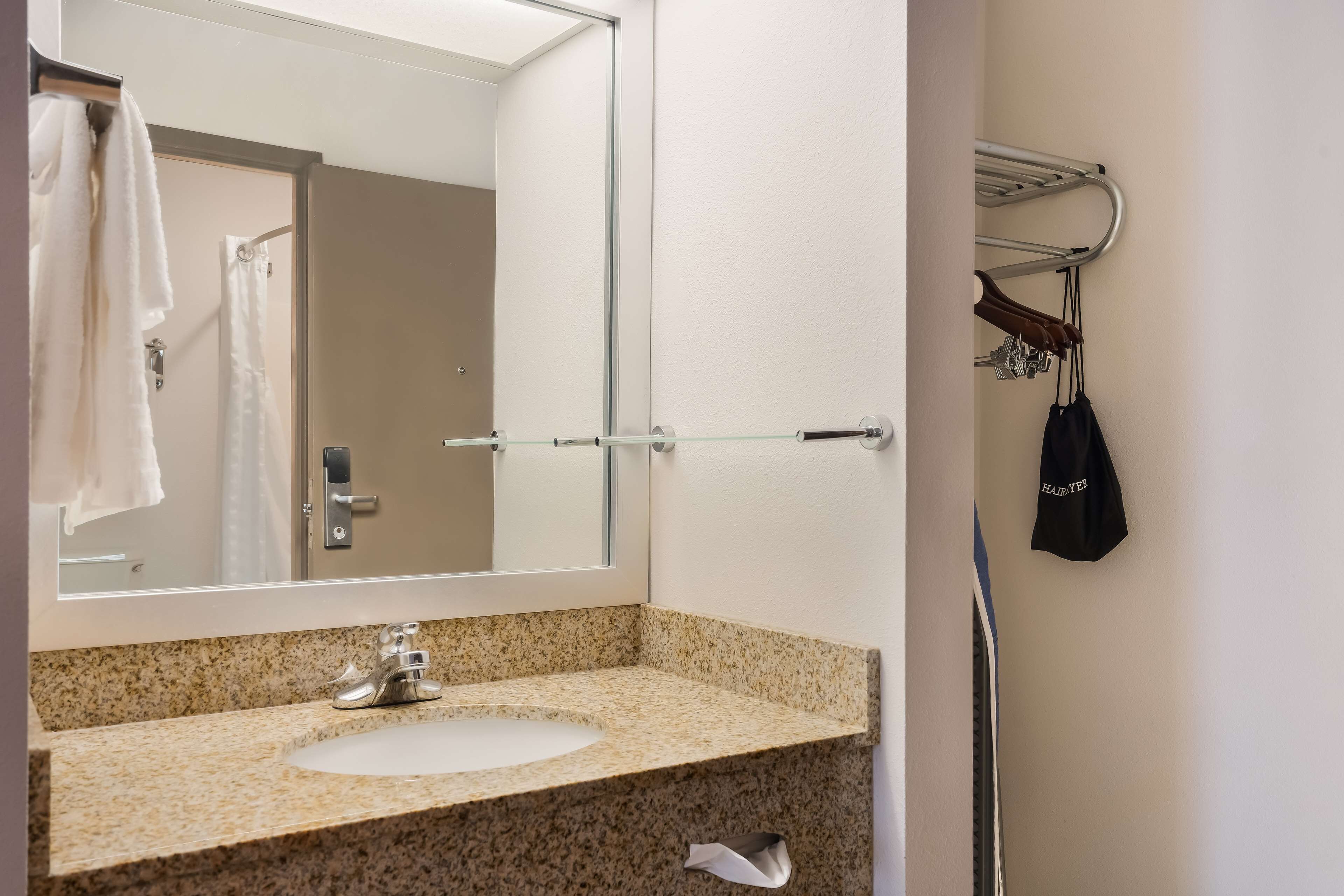 A bathroom with a granite countertop sink, a mirror, and a towel rack with a black bag hanging on it.