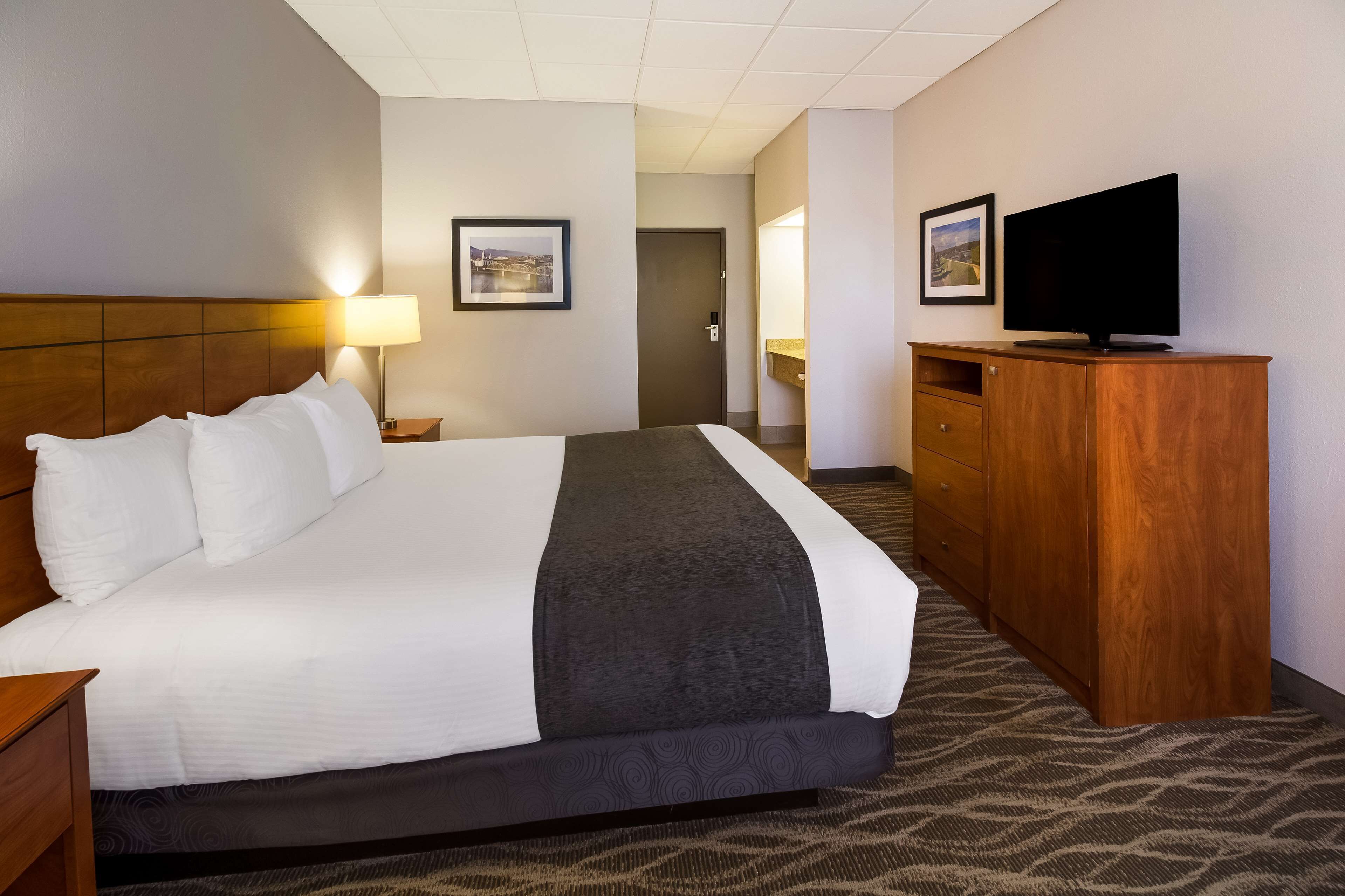A hotel room with a large bed, a wooden dresser, a television, and two framed pictures on the wall.
