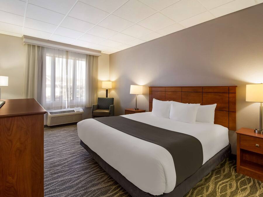 Een hotelkamer met een groot bed, twee nachtkastjes met lampen, een bureau met stoel, een raam met gordijnen en een vloerbedekking.