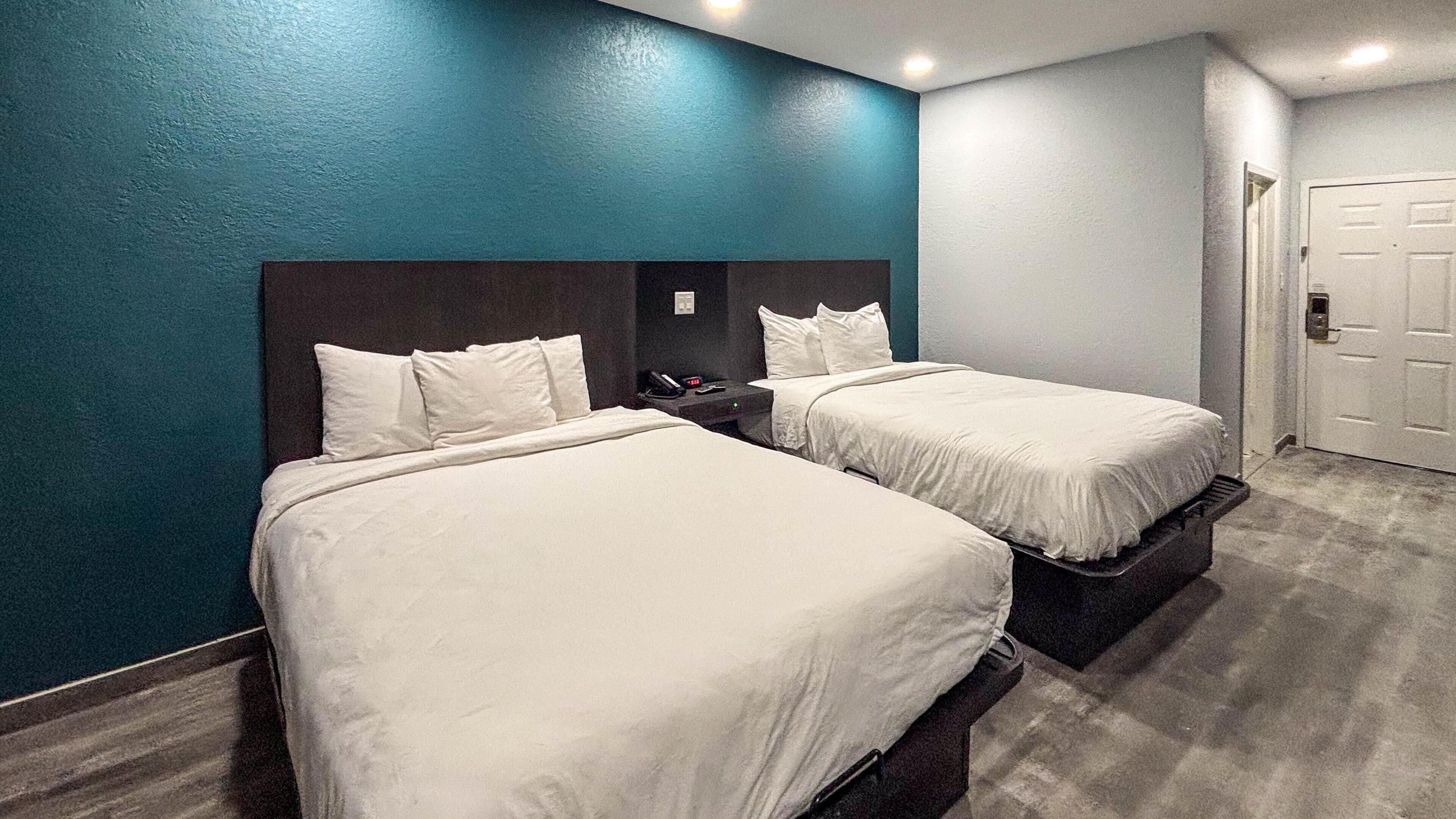 A hotel room with two beds, a dark headboard, a nightstand, and a door.