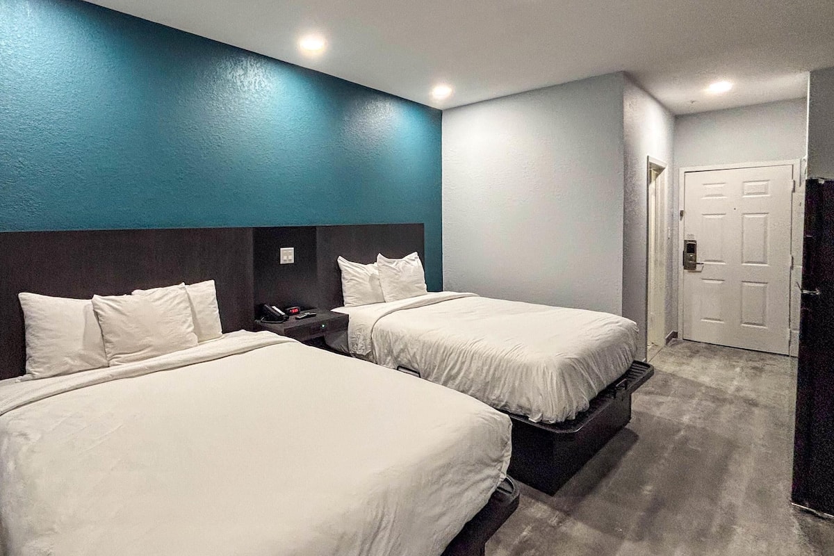 A hotel room with two beds, a dark headboard, and a white door.