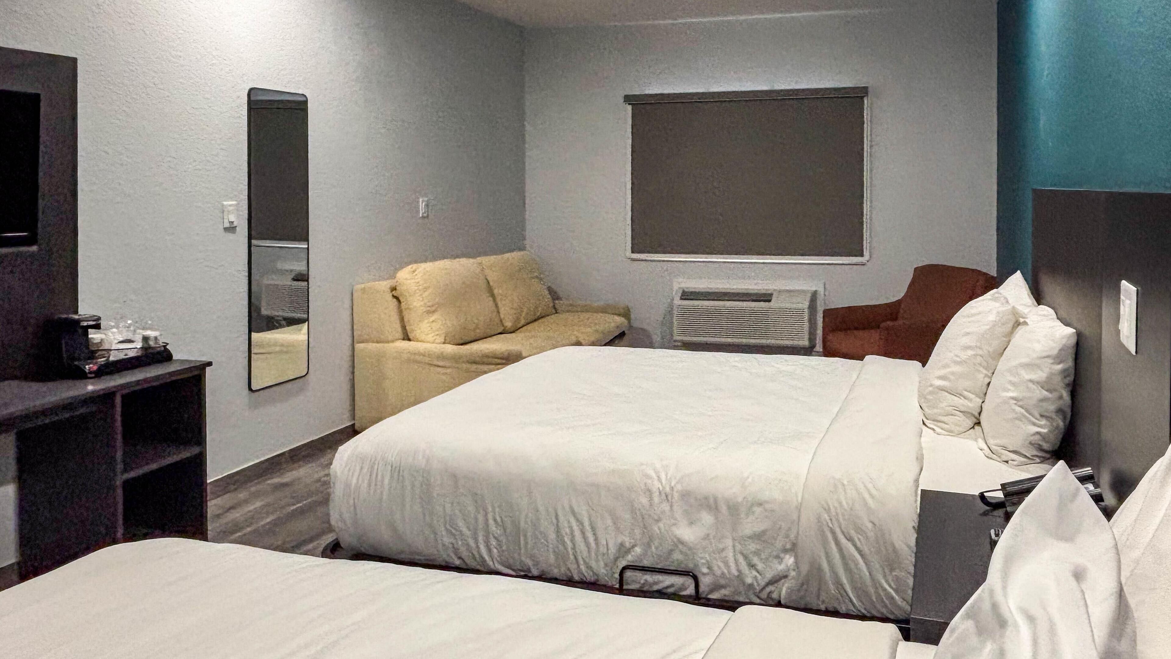 A hotel room with two beds, a sofa, a desk, and a mirror.