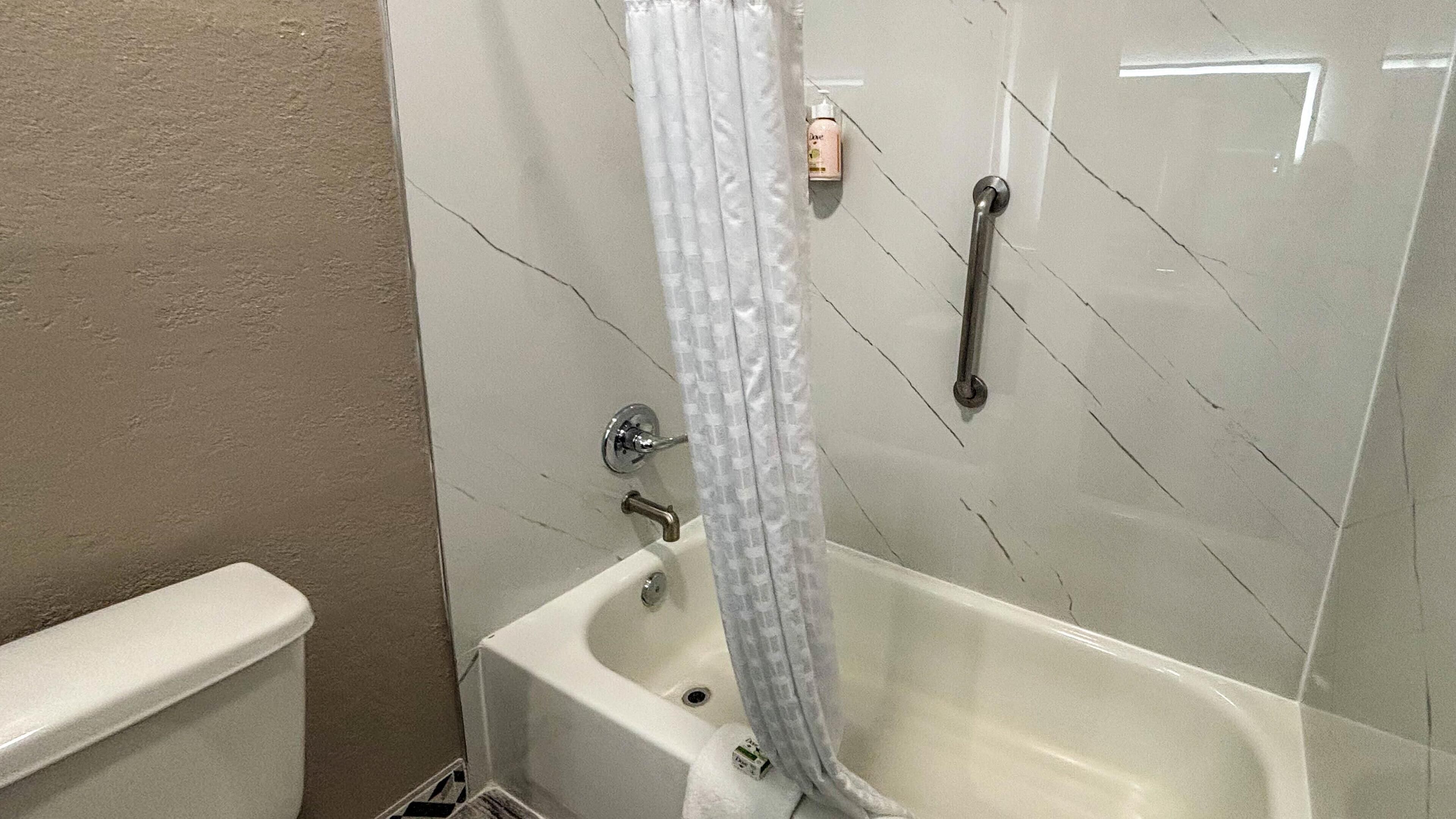 Une salle de bain avec une baignoire, un rideau de douche et une barre d’appui.