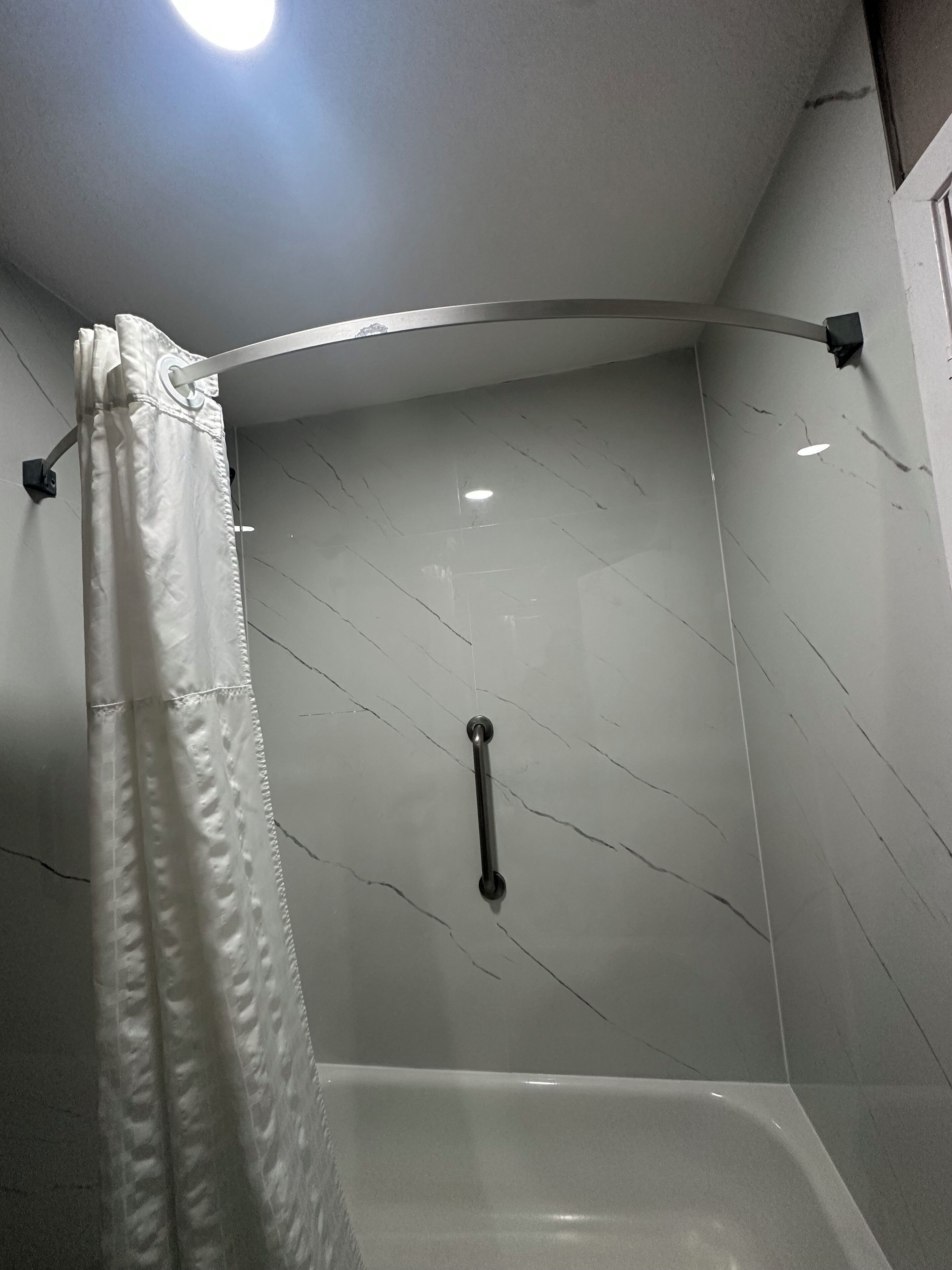 A shower area with a white curtain, a handheld showerhead, and a wall with a marble-like pattern.