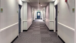 A hotel hallway with carpeted floors, white walls, and doors on both sides.