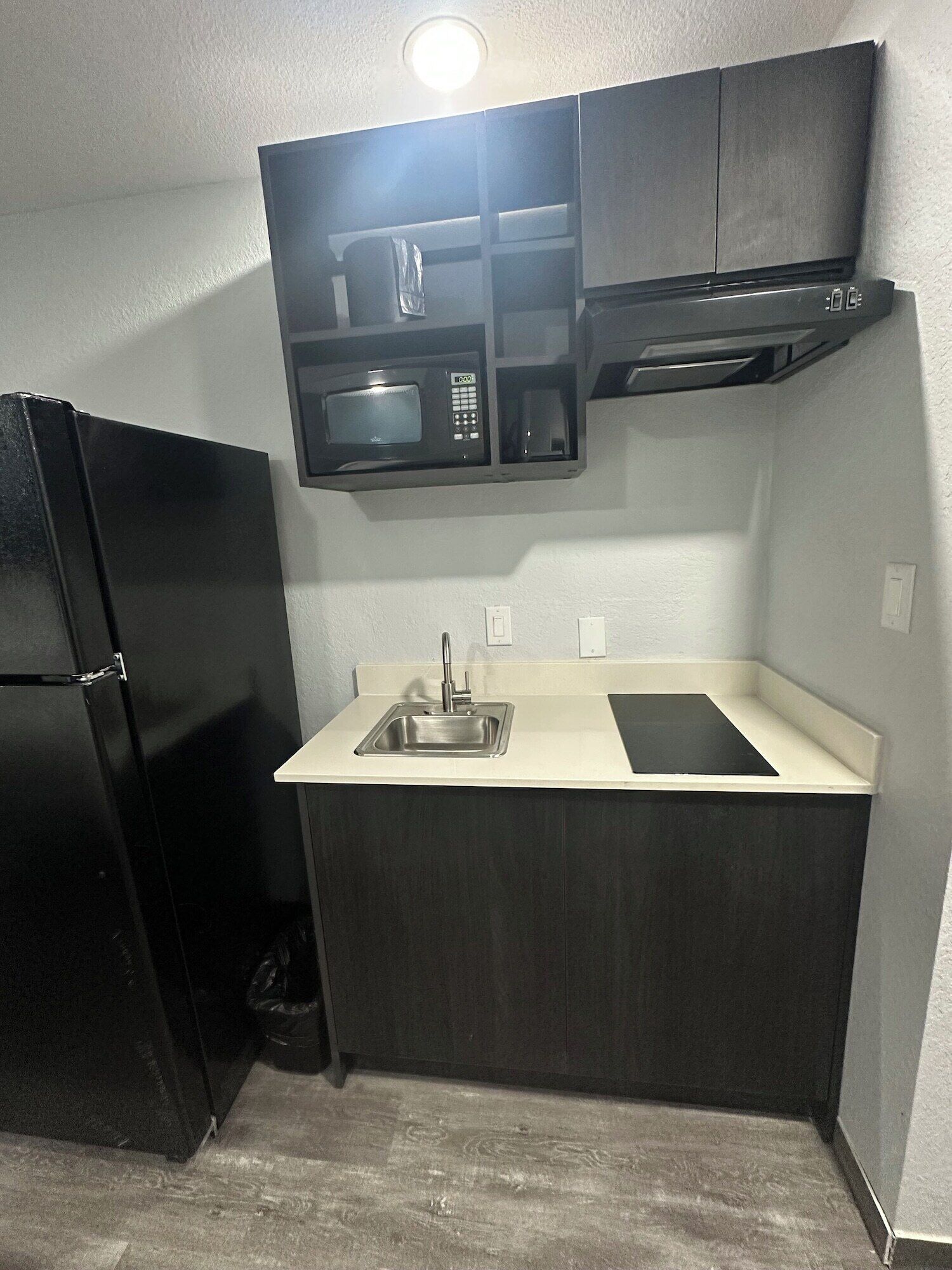 Una cocina compacta con un refrigerador negro, un microondas y un lavamanos.