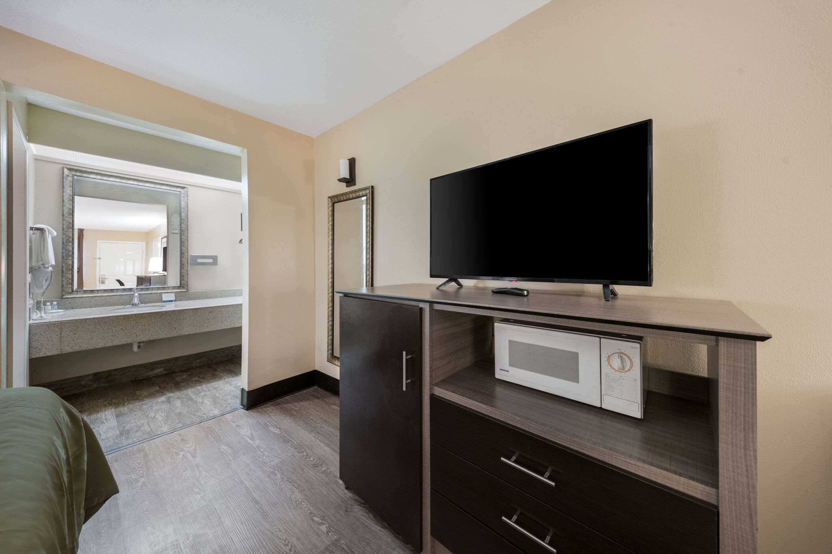 A hotel room with a bed, a TV, a microwave, a mirror, and a small cabinet.