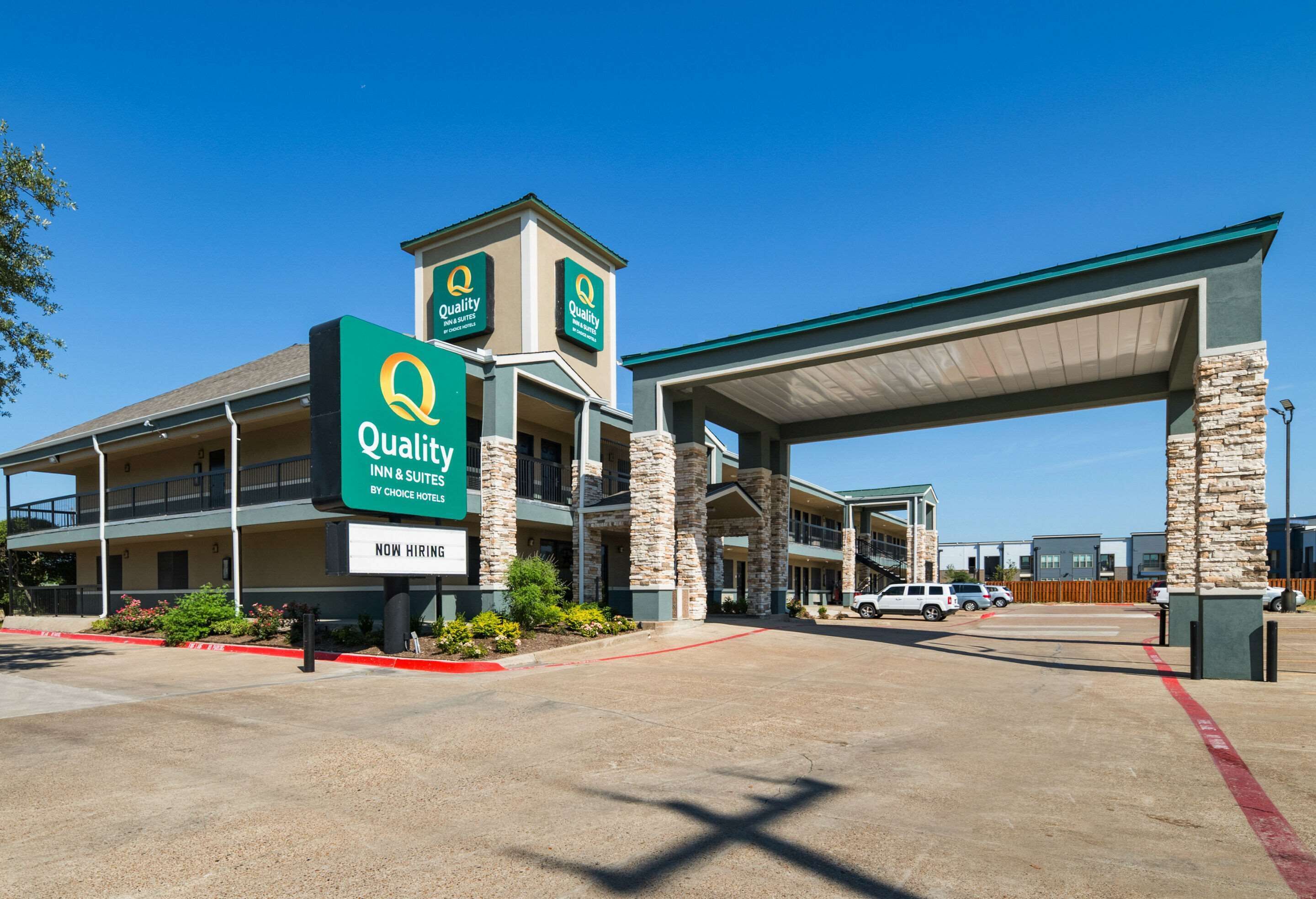 Un établissement Quality Inn & Suites, appartenant à la chaîne Choice Hotels, avec un ciel dégagé, un parking couvert et une station-service bien visible.