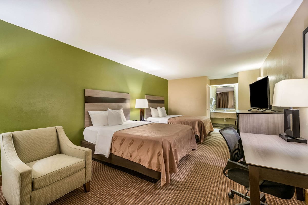 A hotel room with two beds, a desk, a chair, a television, and a window.