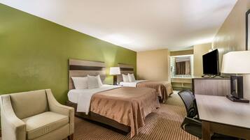 A hotel room with two beds, a desk, a chair, a television, and a window.