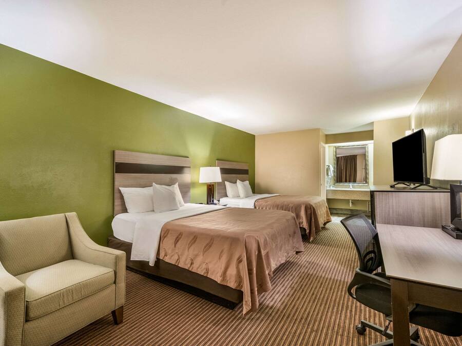 A hotel room with two beds, a desk, a chair, a television, and a window.