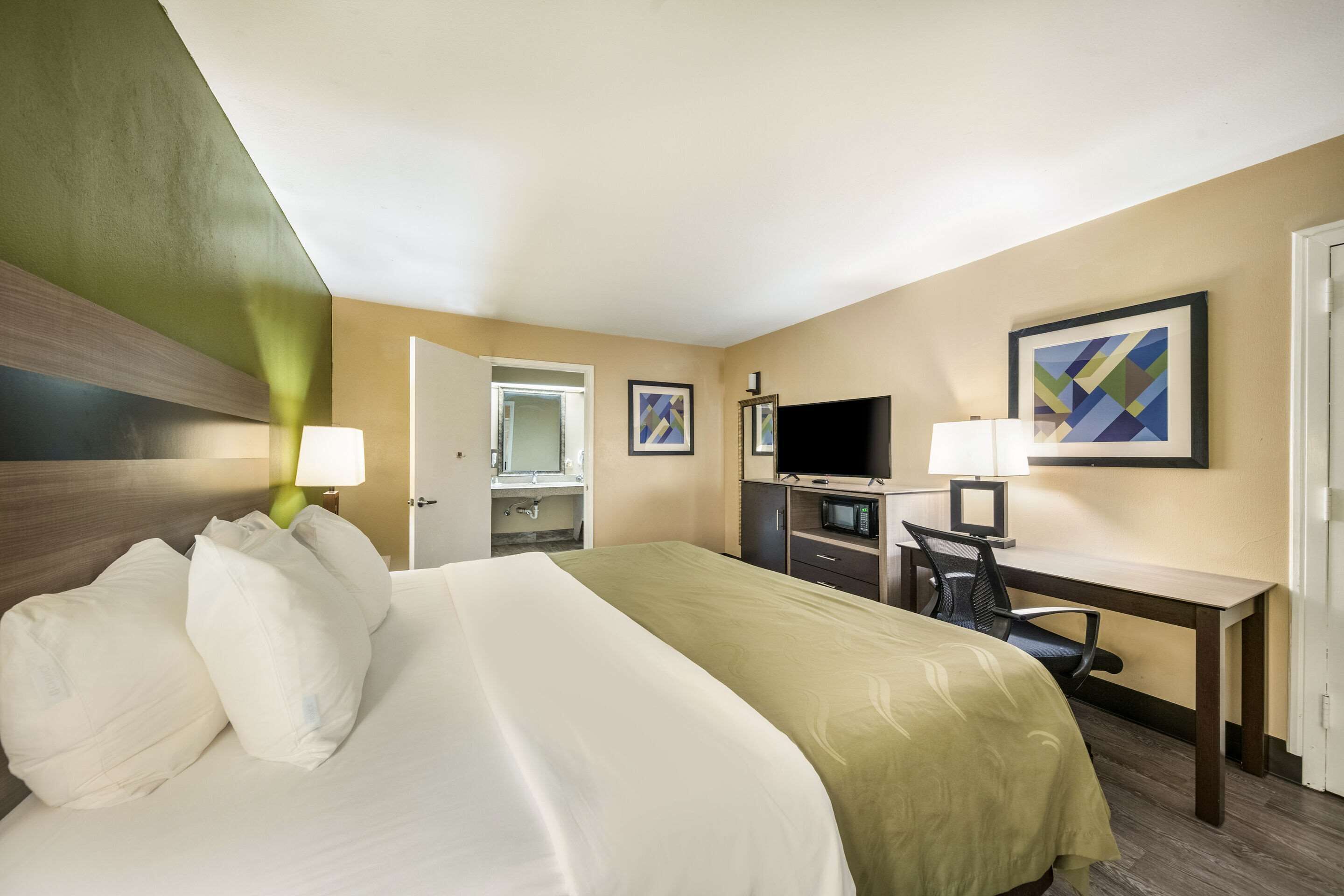 Une chambre d’hôtel avec un grand lit, un bureau avec un ordinateur, une télévision et un miroir.