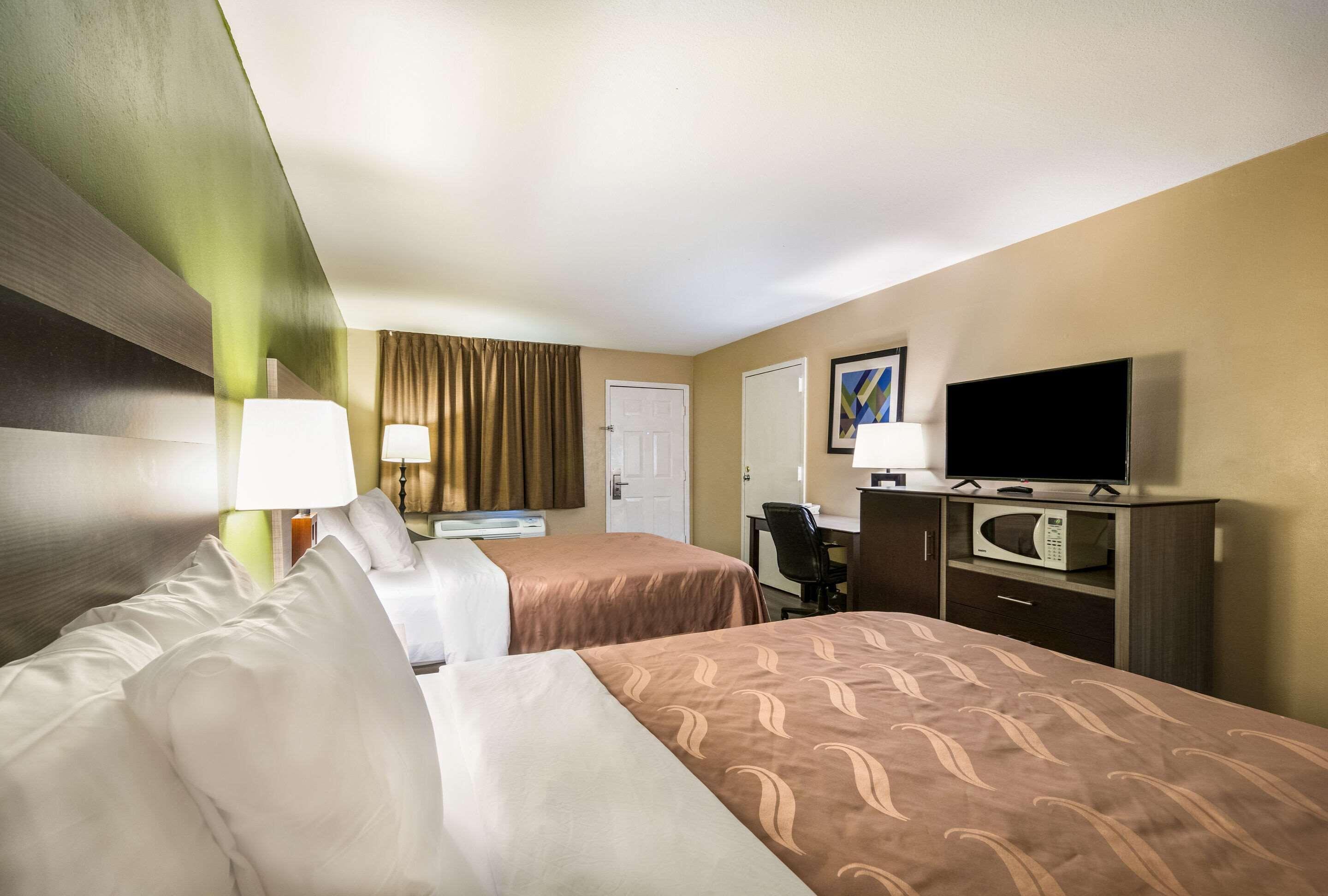Habitación de hotel con dos camas, un escritorio, un televisor y un microondas.