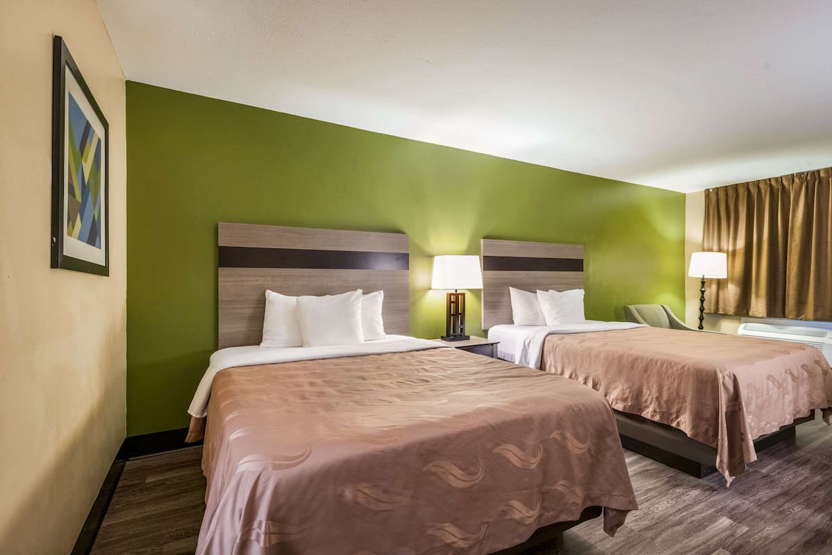 A hotel room with two beds, green walls, and a framed picture on the left.
