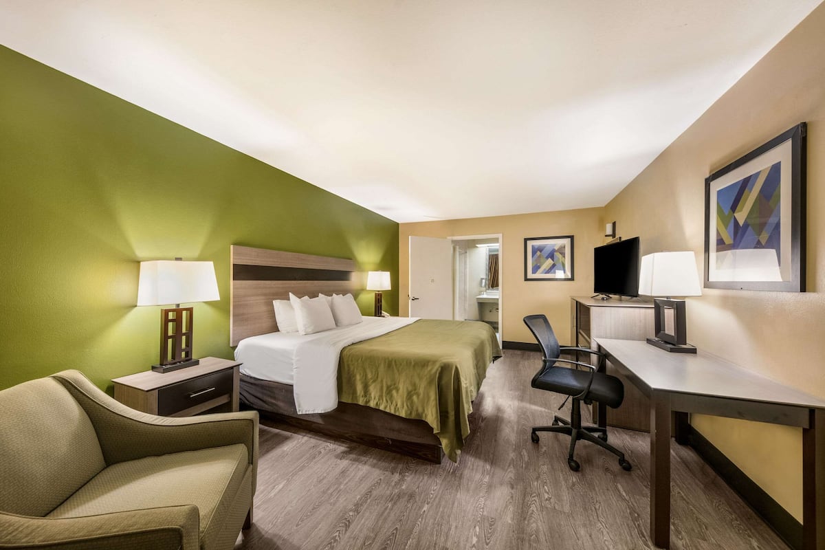 A hotel room with a bed, a desk, a chair, a nightstand, and a TV.