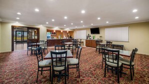 A hotel dining area with multiple tables and chairs, a bar, and a television on the wall.