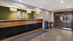 A reception desk with a sign reading "Quality by Choice Hotels," a digital screen, and a wooden counter.