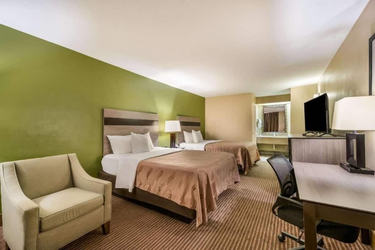 A hotel room with two beds, a desk, a chair, and a television.