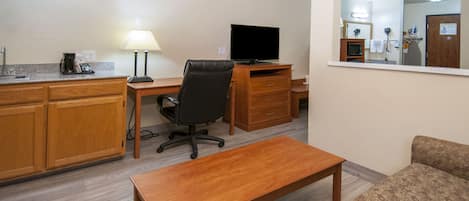 Une chambre d’hôtel compacte comprenant un coin cuisine, un bureau en bois avec une chaise, une télévision, un miroir et un canapé.