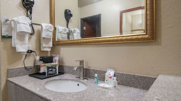 A bathroom with a sink, mirror, hairdryer, and toiletries.