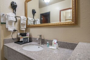 A bathroom with a sink, mirror, hairdryer, and toiletries.