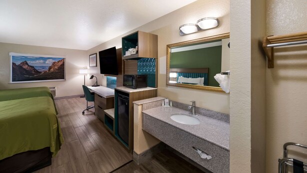 A hotel room with a bed, desk, microwave, sink, and a large mirror.