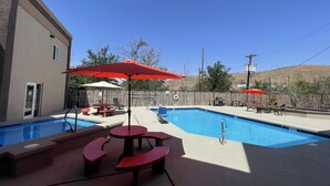 A backyard with two swimming pools, red picnic tables, and umbrellas.