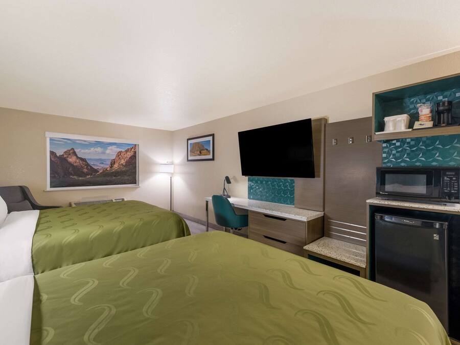 A hotel room with two beds, a desk, a TV, a microwave, and a refrigerator.