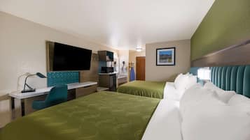 A hotel room with two beds, a desk, a chair, a TV, and a kitchenette.