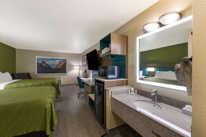 A hotel room with two beds, a desk, a microwave, a sink, and a large mirror.