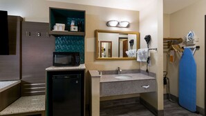 A compact bathroom with a sink, mirror, and a microwave on a countertop.