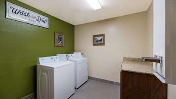 A laundry room with two white front-loading washers and dryers, a wooden vanity with a sink, and a green wall.