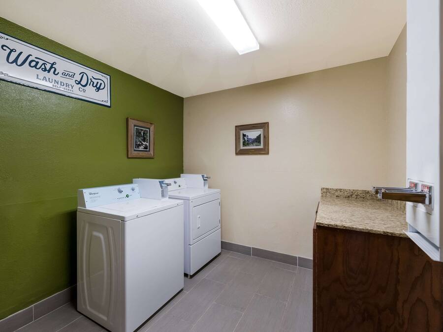 A laundry room with two white front-loading washers and dryers, a wooden vanity with a sink, and a green wall.